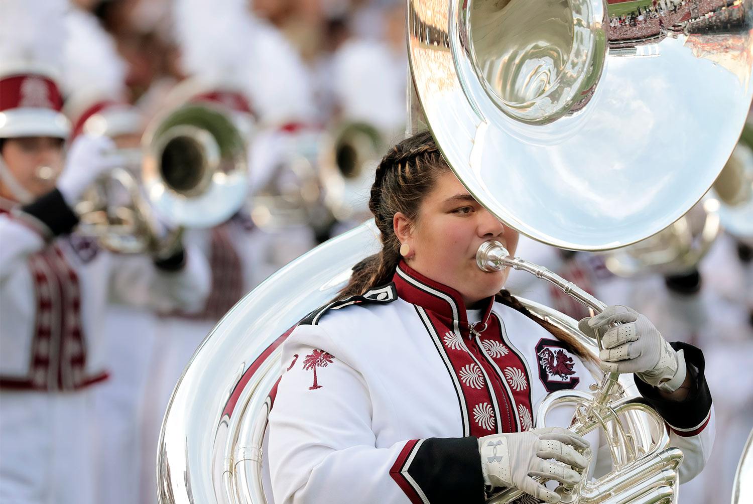 Marching band member playing the sousaphone dressed in full uniform at a football game.  