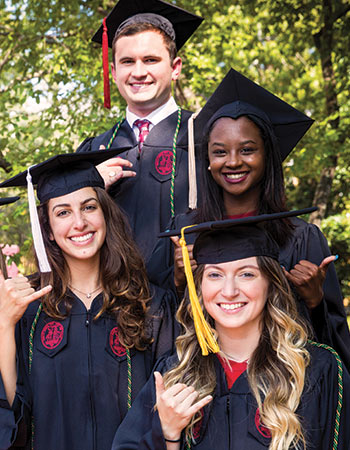 四个学生在毕业帽和礼服对着镜头微笑着举起马刺的姿态。